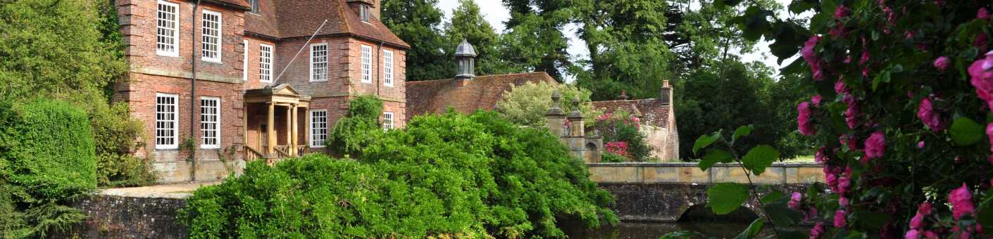 The beautiful Groombridge Place House surrounded by vibrant green trees, water 